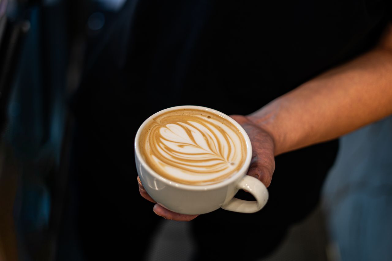 Close-up of a baristas hand holding a latte featuring intricate latte art.