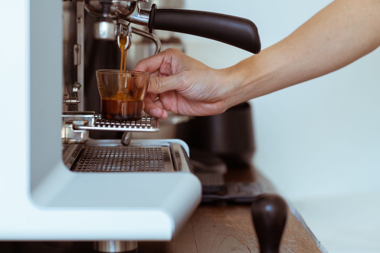 Side view of crop unrecognizable worker pouring fresh espresso into cup from portafilter while preparing coffee using coffee machine in modern cafe